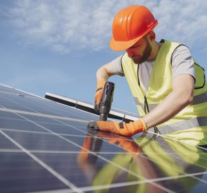 Male worker with solar batteries. Man in a protective helmet. Installing stand-alone solar panel system.
