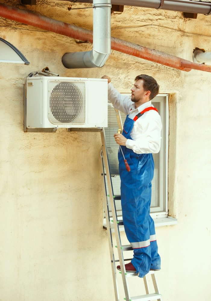 HVAC technician working on a capacitor part for condensing unit. Male worker or repairman in uniform repairing and adjusting conditioning system, diagnosting and looking for technical issues.