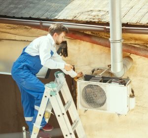 HVAC technician working on a capacitor part for condensing unit. Male worker or repairman in uniform repairing and adjusting conditioning system, diagnosting and looking for technical issues.